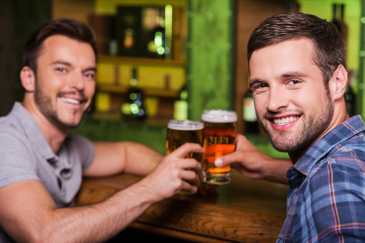 Two smiling men clinking glasses of beer at a bar
