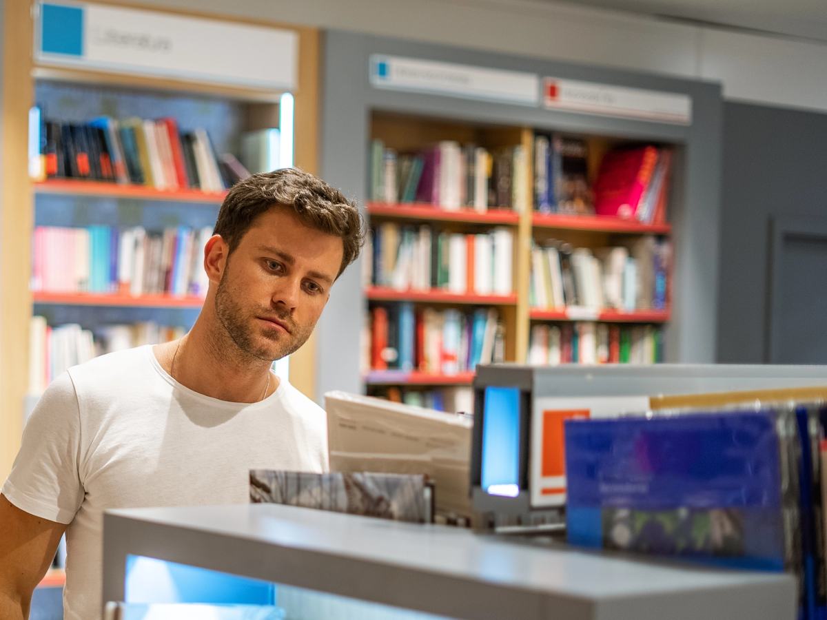 A handsome man in a white T-shirt looking over the books in a bookstore