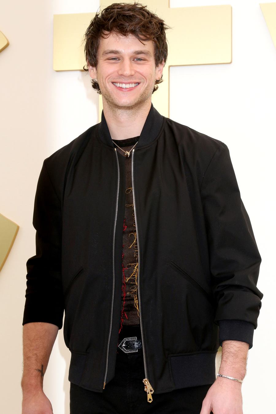 Brandon Flynn smiling in a black bomber jacket at the Apple TV Press Day