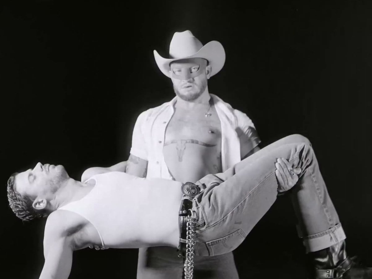 Orville Peck in a cowboy hat carrying François Arnaud in his arms in black and white