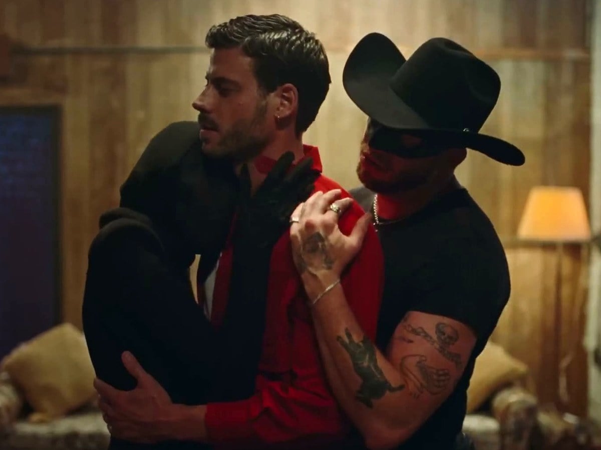 Orville Peck in a black cowboy hat, mask and T-shirt lifting François Arnaud, who wears a red jacket, in the How Far Will We Take It? music video