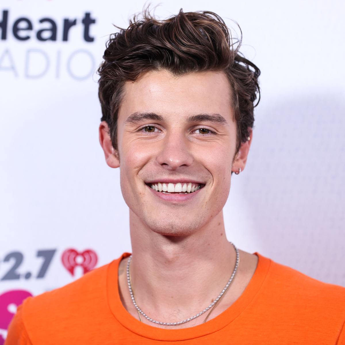Shawn Mendes smiling in an orange T-shirt and silver chain at the iHeartRadio Wango Tango