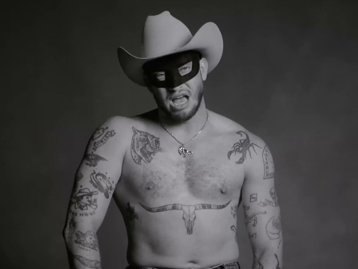A shirtless, tattooed Orville Peck in his mask and white cowboy hat