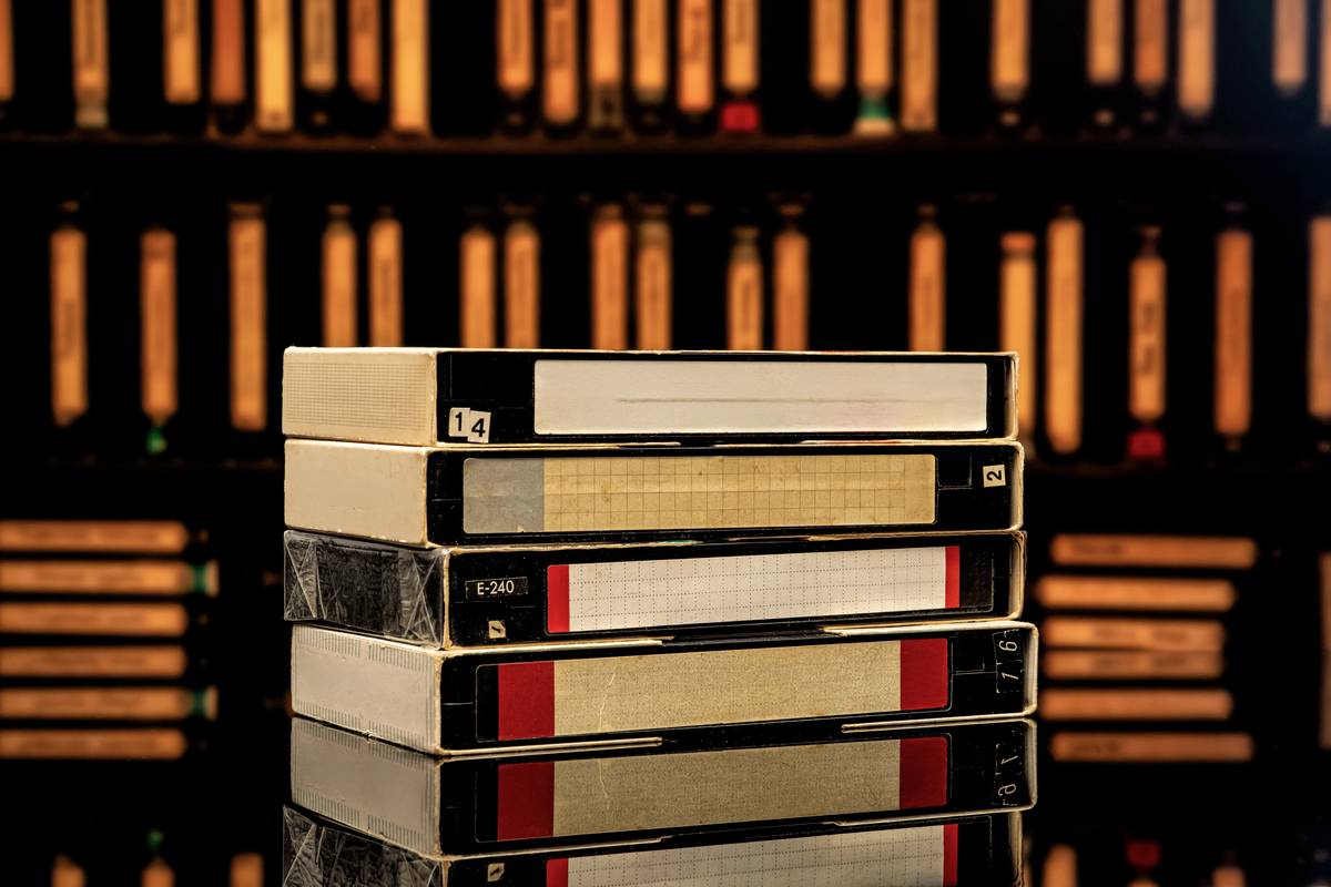 A stack of vintage VHS videotapes in front of a shelf of more tapes