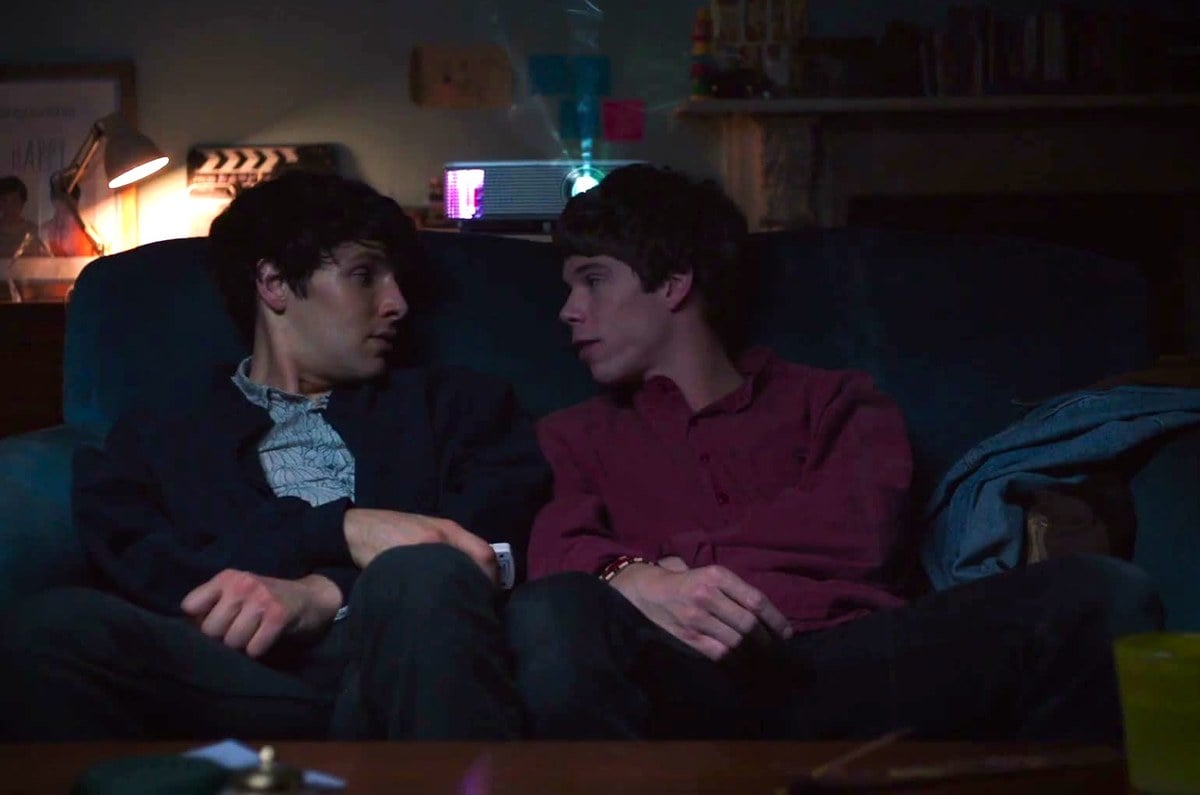 Colin Morgan and Phénix Brossard sitting close together on a sofa at night in Benjamin