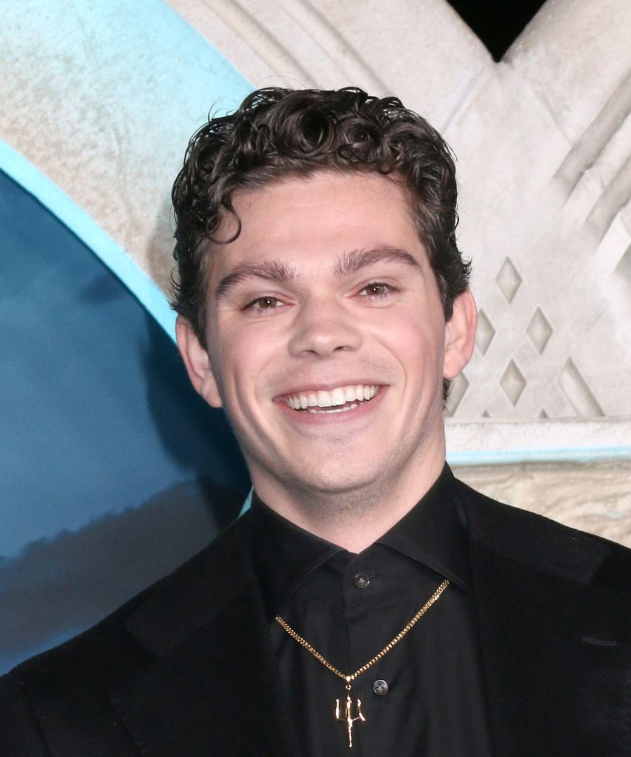 Daniel Diemer smiling in a black suit and shirt with a gold trident necklace