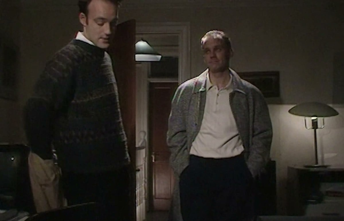Michael Cashman and Nicholas Donovan as Colin and Guido standing in a flat in EastEnders in 1989