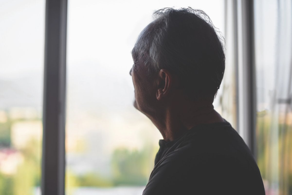 Elderly man silhouetted at a window, looking out