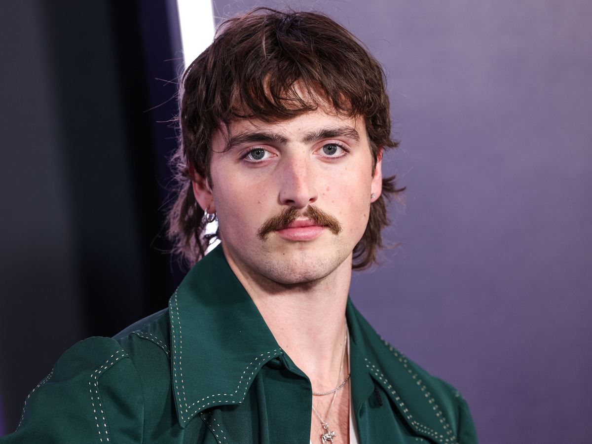 Benson Boone with a mullet and mustache in a green jacket with white stitching