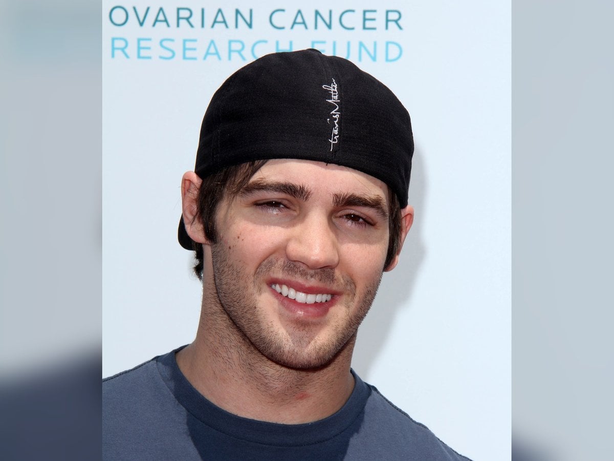 Steven R. McQueen smiling in a backwards black cap and gray T-shirt