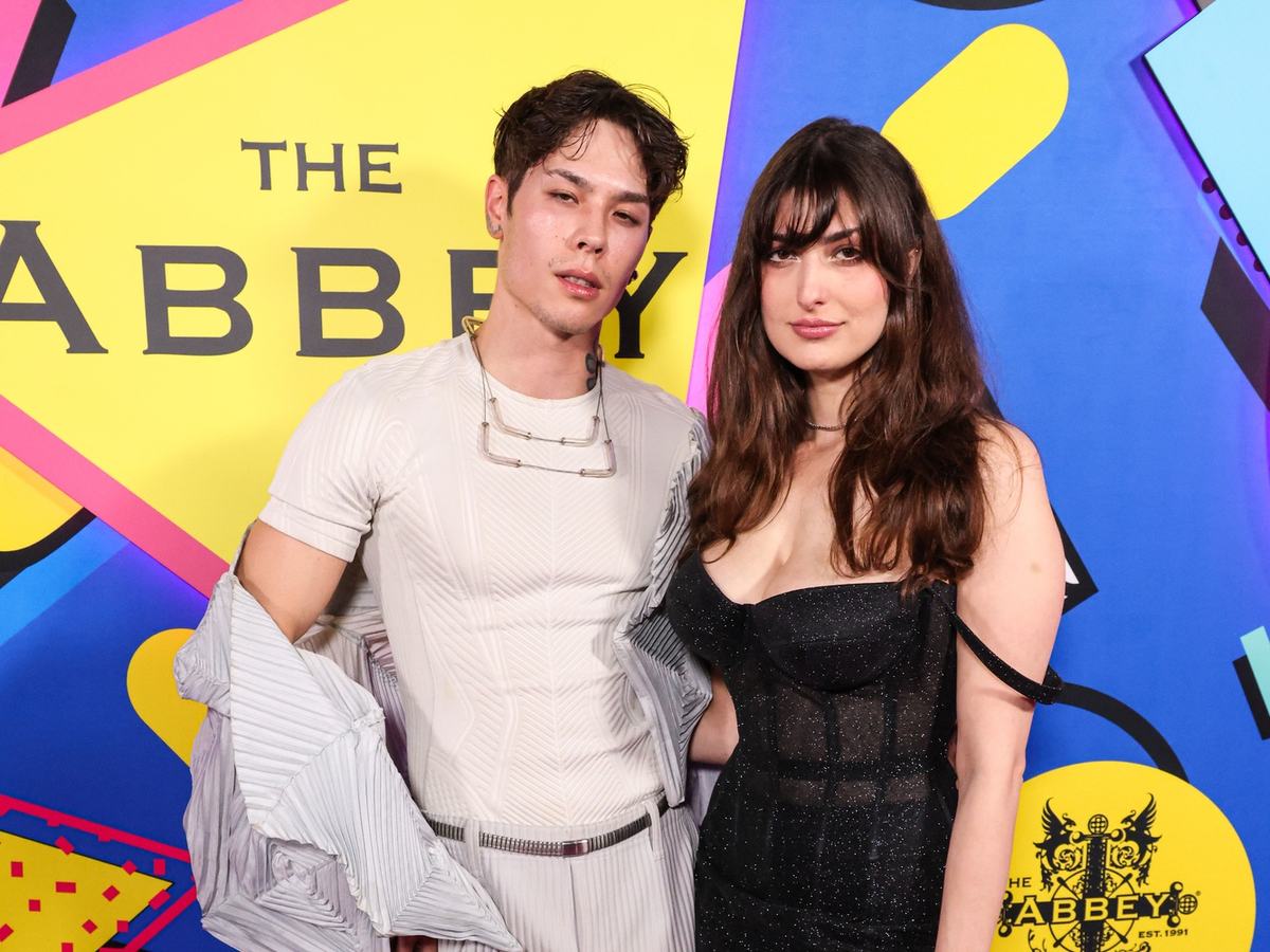 Kaeden Kalaqtic in a white pleated outfit and Rachel Levin in a black corset dress on the pink carpet in front of The Abbey backdrop