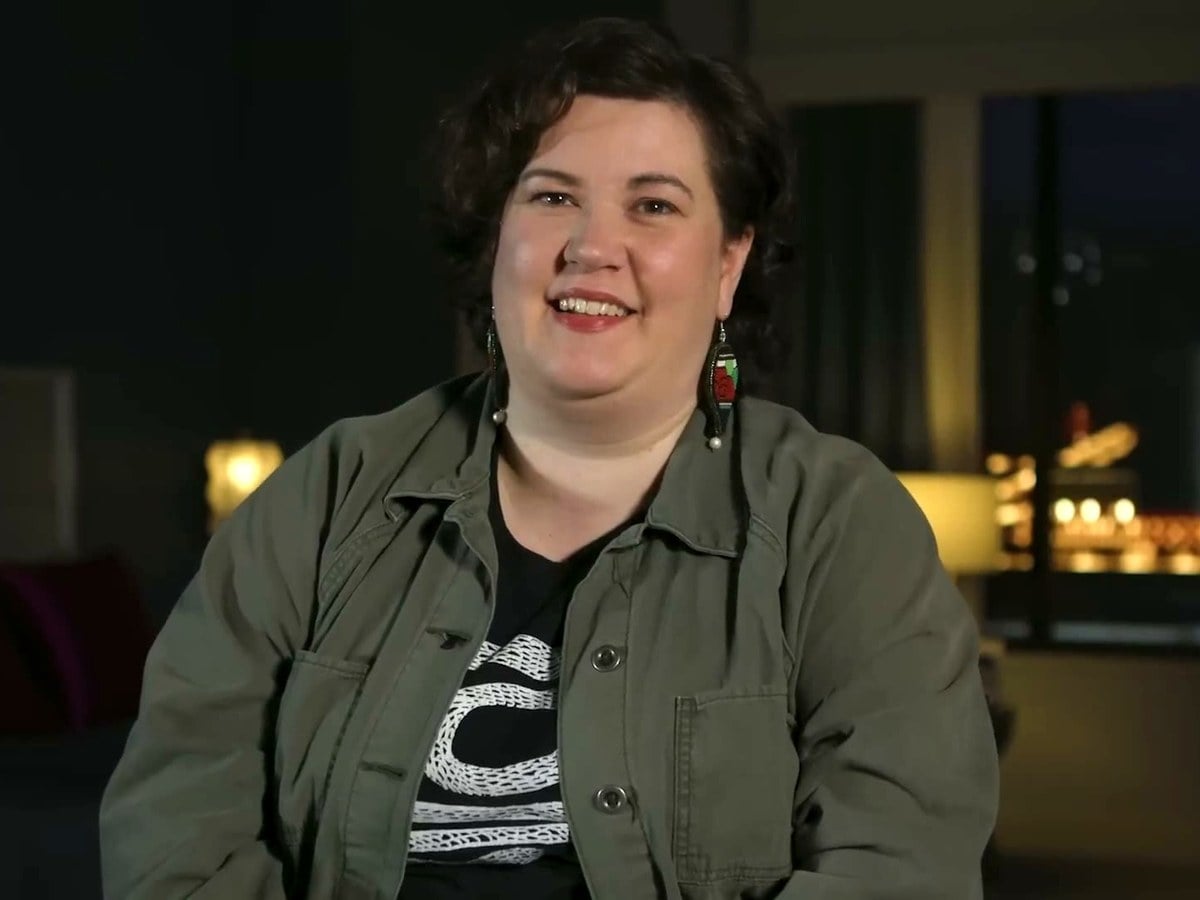 Rachel Reid smiling in an olive jacket during an interview in a dimly lit hotel room
