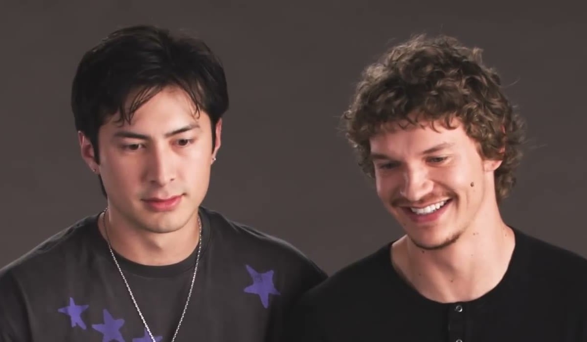 Hudson Williams and Connor Storrie smiling as they watch a scene together