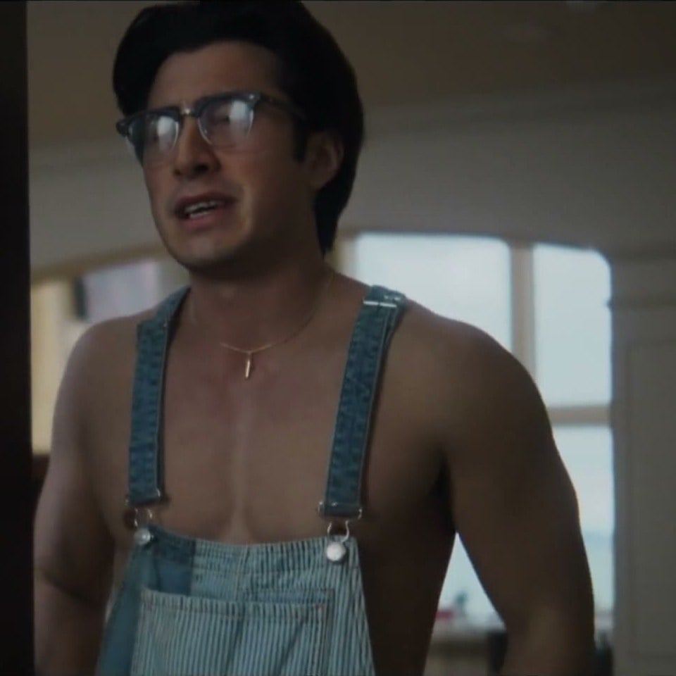 Hudson Williams as Logan, wearing glasses and denim overalls with no shirt underneath