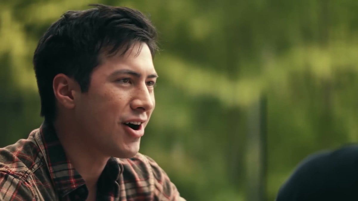 Hudson Williams as Shane in a plaid shirt, smiling outdoors at the cottage