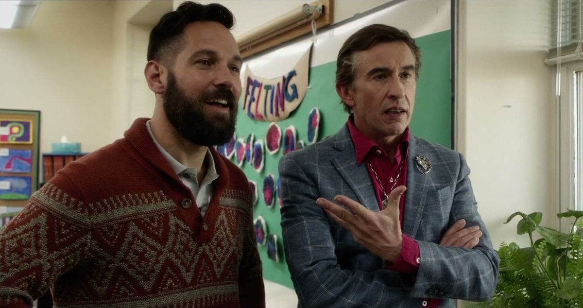 Paul Rudd in a patterned sweater and Steve Coogan in a checked blazer standing in a school classroom in Ideal Home