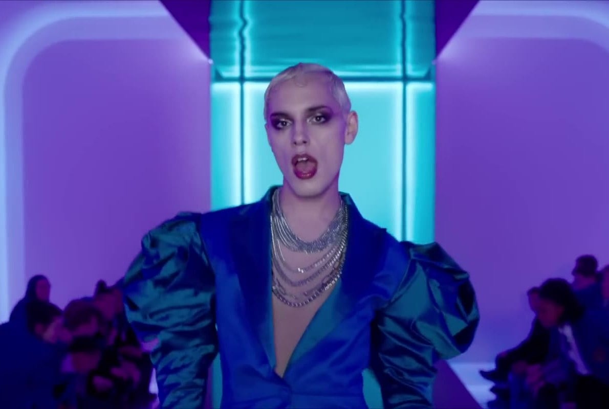 Max Harwood in full drag and a blue satin jacket performing on a neon-lit catwalk in Everybody’s Talking About Jamie