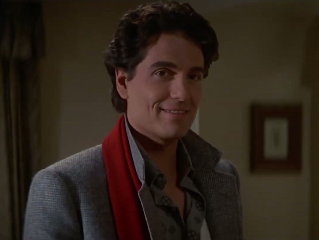 Chris Sarandon as Jerry Dandrige, smiling in a grey jacket and red scarf, in Fright Night