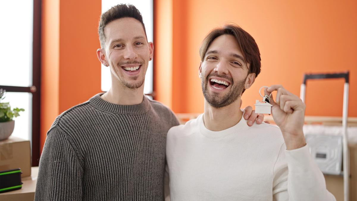 Two laughing men hugging and holding up a set of house keys in a new home