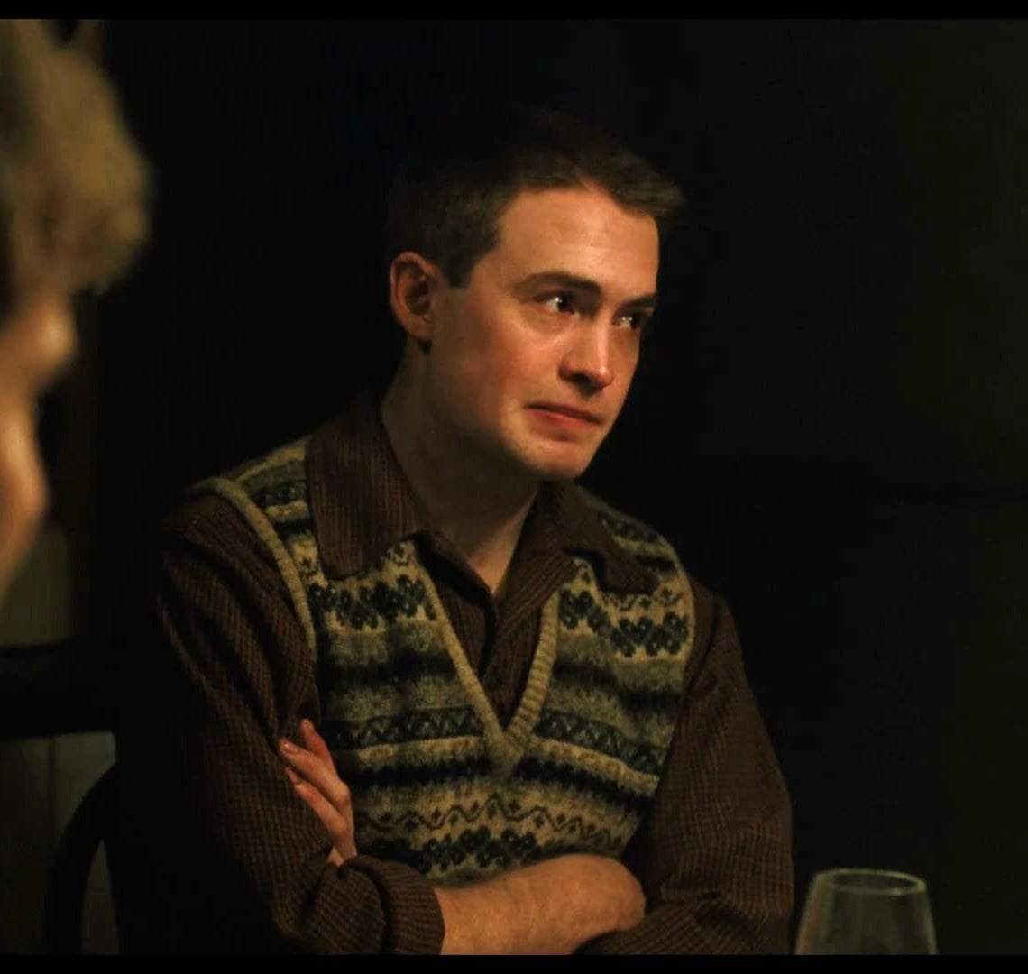 Kit Connor as Tommy in a patterned sweater vest at the family dinner table