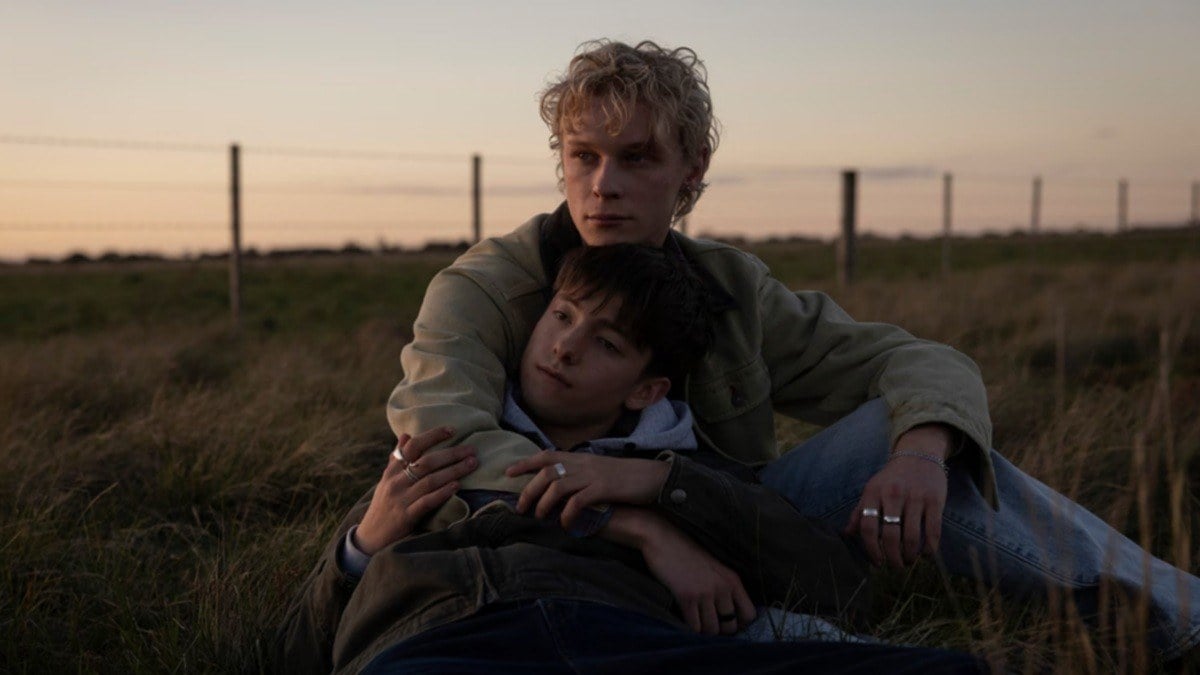 Stacy Clausen holding Joe Bird as they sit together in tall grass at sunset in Leviticus