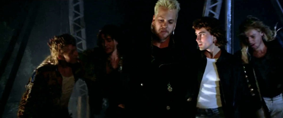 Kiefer Sutherland as David in the middle of the Lost Boys gang, with Jason Patric beside him, walking across a train bridge at night