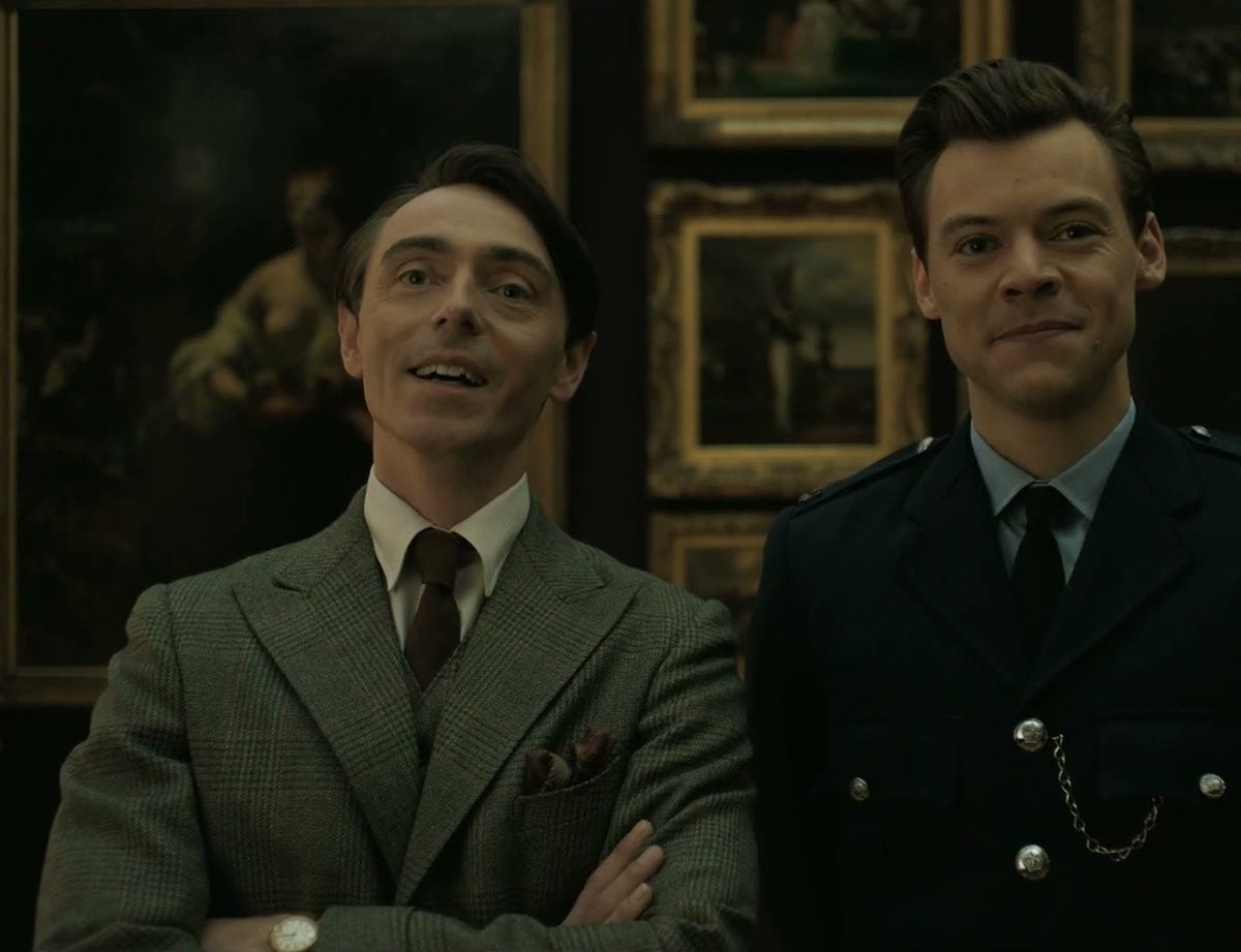 David Dawson in a tweed suit and Harry Styles in a 1950s police uniform smiling in a museum in My Policeman