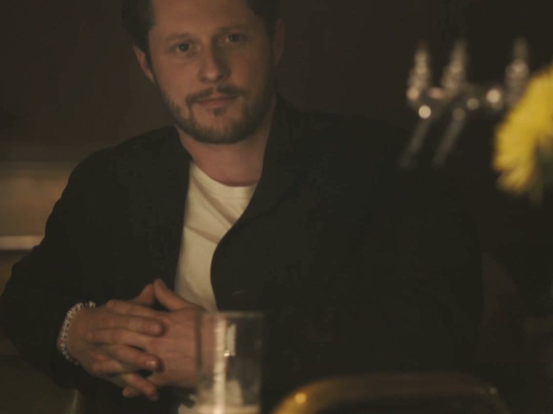 Noah Reid as private investigator Rapp, sitting at a dimly lit bar with his hands clasped