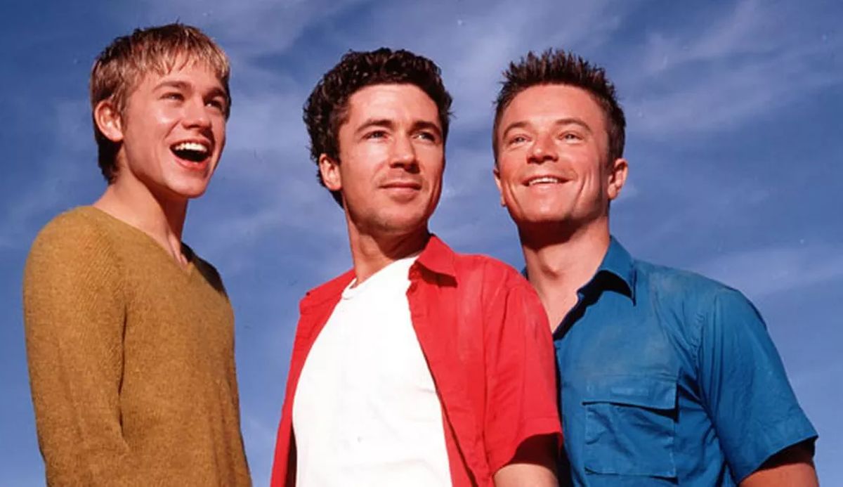 The three leads of the British Queer as Folk smiling against a blue sky