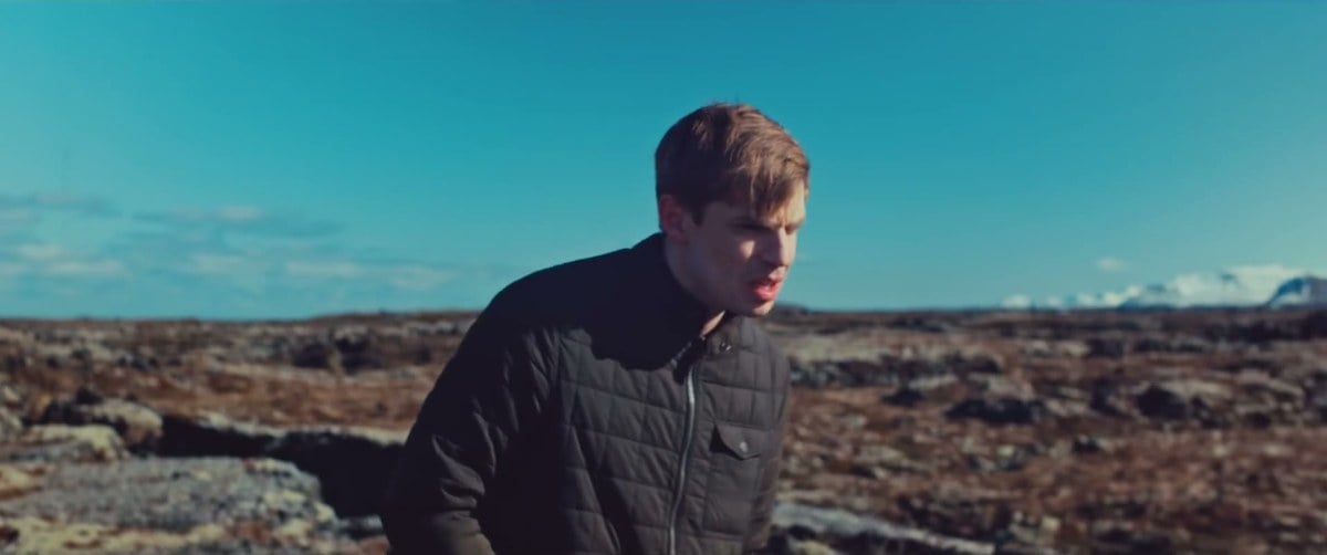 A man in a dark jacket alone on a vast Icelandic lava field under a blue sky in Rift