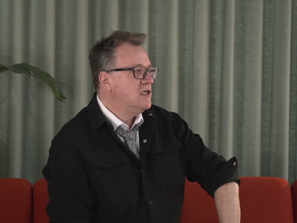 Russell T Davies in glasses and a dark jacket, speaking during an interview about Tip Toe
