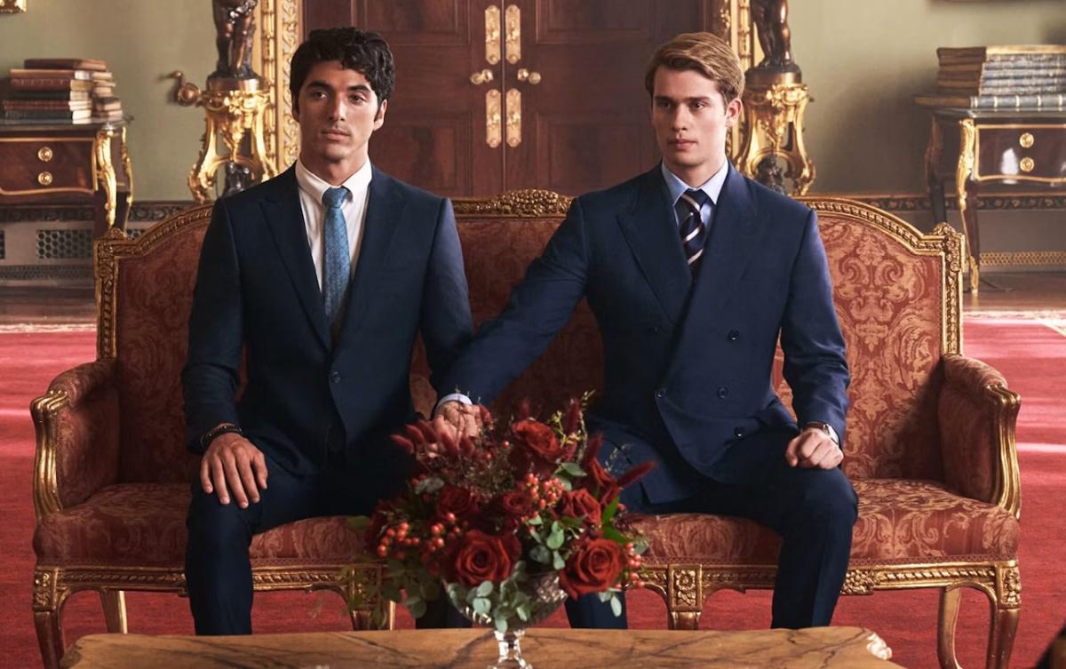 Taylor Zakhar Perez and Nicholas Galitzine in navy suits sitting side by side on a gilded palace sofa in Red, White and Royal Blue