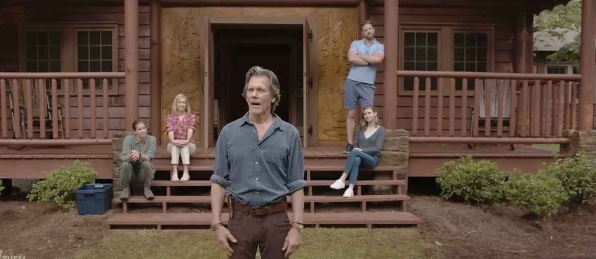 Kevin Bacon as camp owner Owen Whistler standing in front of a log cabin, with campers sitting on the steps behind him