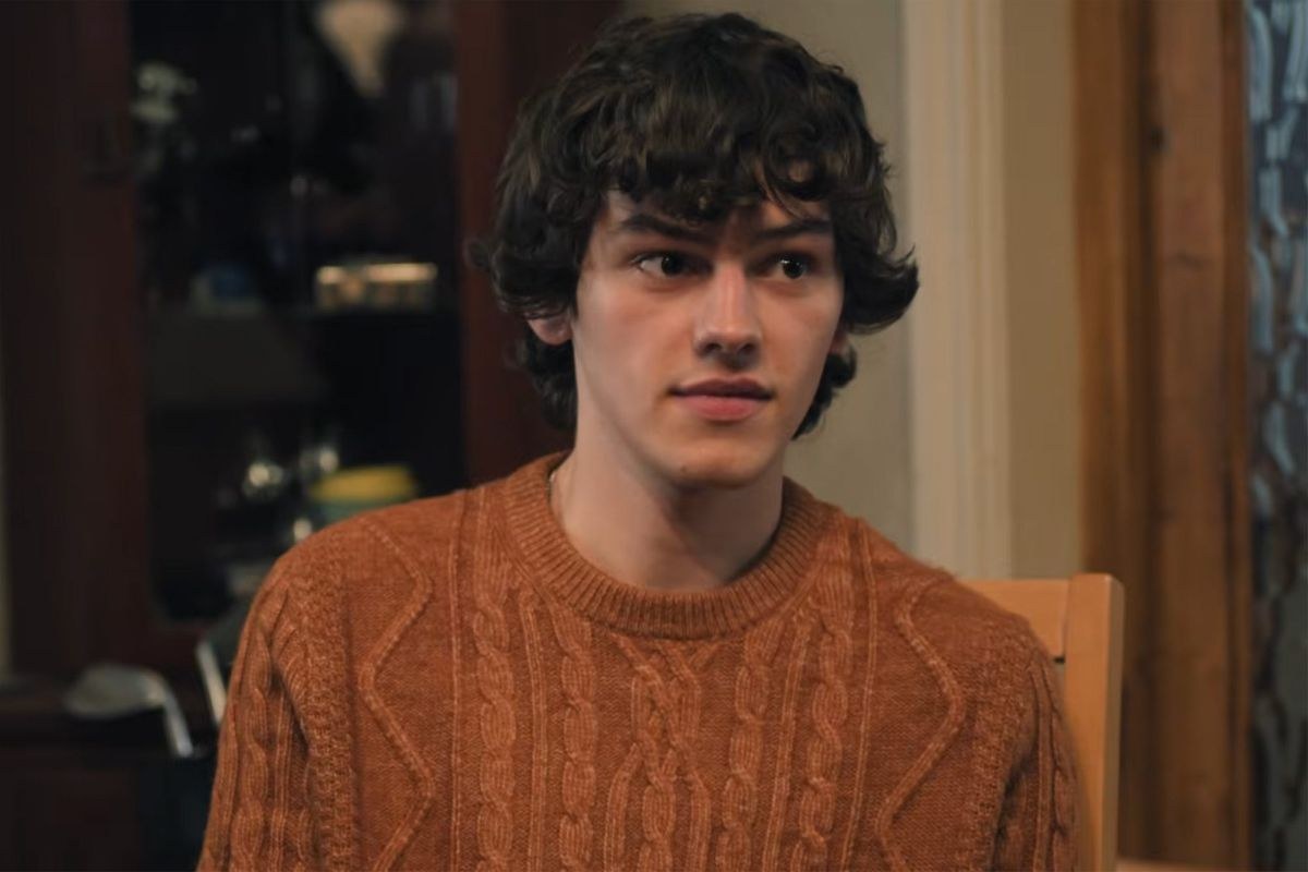 Jackson Connor as George in Tip Toe, wearing a rust cable-knit sweater at a kitchen table
