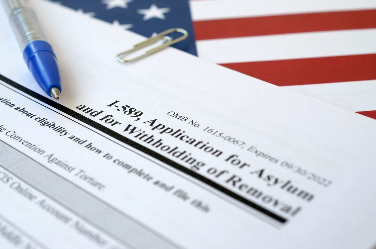 A blank US I-589 Application for Asylum form lying on an American flag with a blue pen