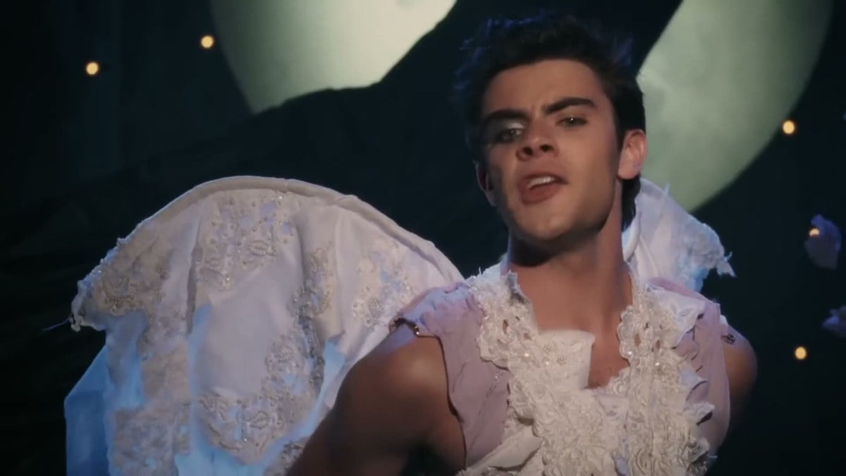 Tanner Cohen in a white fairy costume with wings singing under a giant moon in Were the World Mine